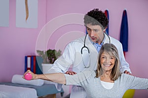 Physiotherapist assisting senior woman to lift dumbbellÂ 